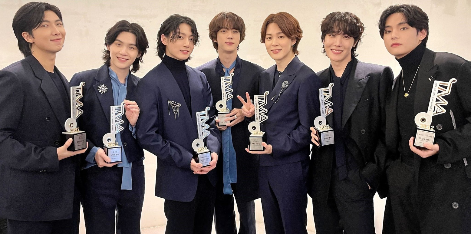 An emotional photo of a K-Pop group tearfully celebrating on stage after winning a 'Daesang' (Grand Prize) at a major music awards show.