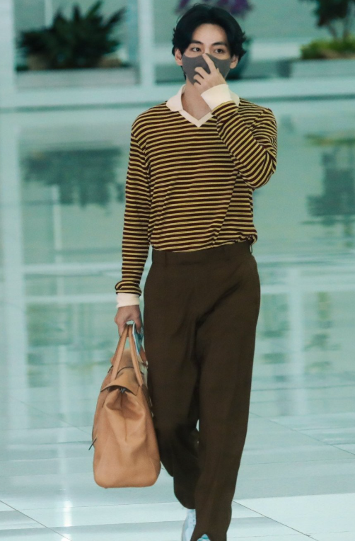BTS's V walking through the airport, embodying his unique and artistic fashion sense with a comfortable yet high-fashion outfit.
