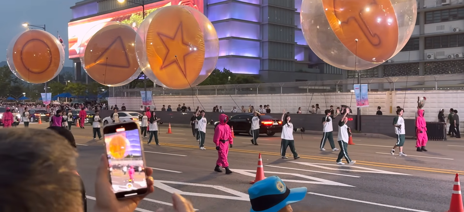 A crowd of people in Seoul at night, gathered around a Squid Game themed event, with faces showing a mix of excitement and curiosity, illustrating the cultural phenomenon.