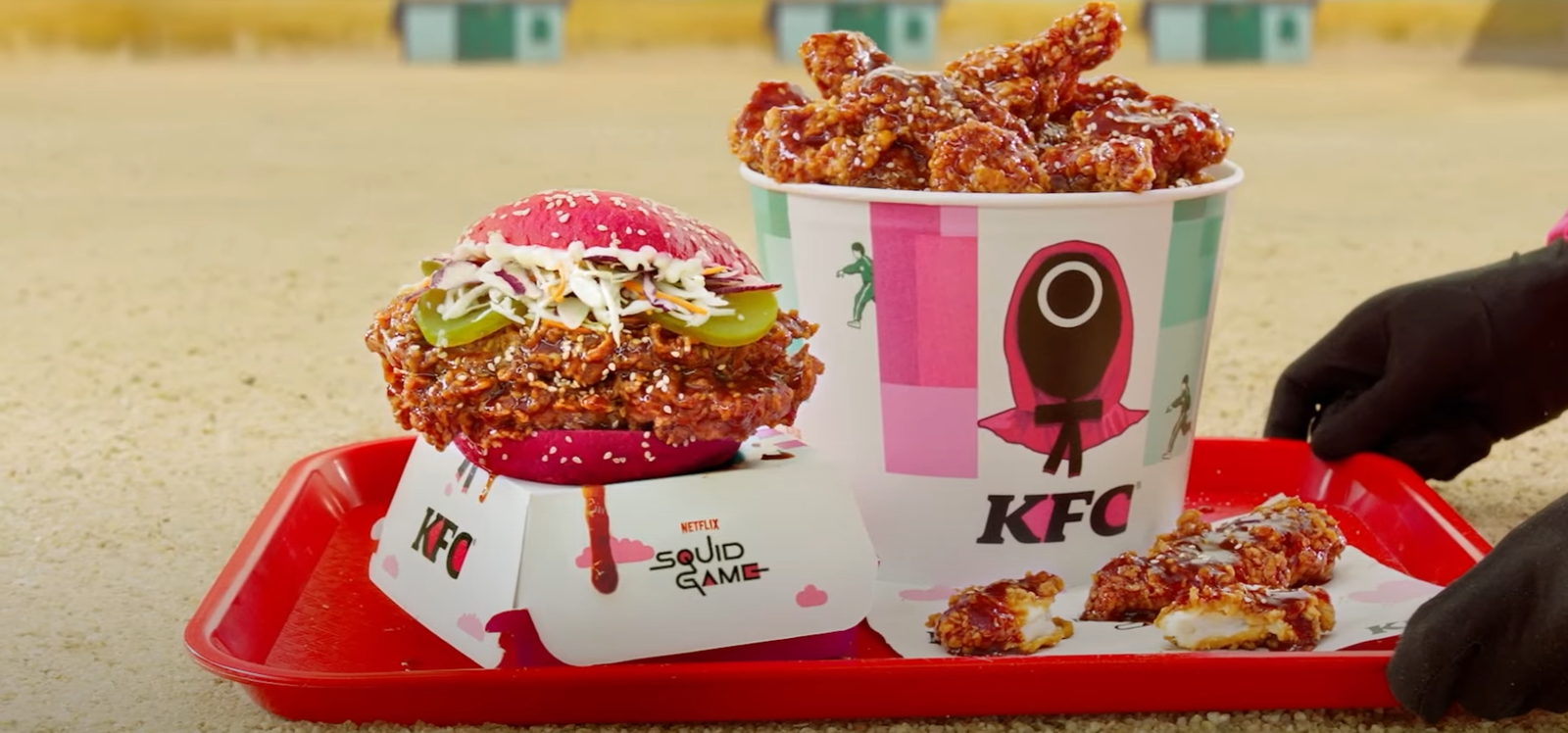 A photo of the special KFC Squid Game meal in Korea, featuring a vibrant pink burger bun on a tray, with themed restaurant packaging in the background.
